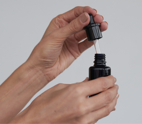 Hand holding open bottle of face oil showing the pipette