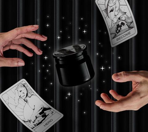 Black jar of silver face cream with hands reach to it from either side, surrounded by illustrated stars and a floating archetype card