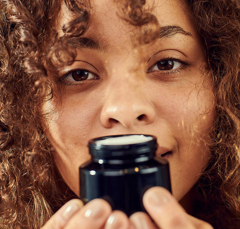 Lady holding an open jar of silver face cream in front of her face